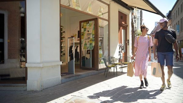 A man and a woman carrying shopping bags walk down a shopping street