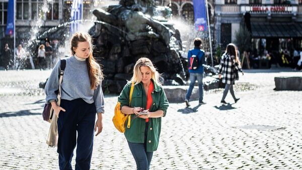 Two girlfriends walk across the main market with guidebook in hand Historic Antwerp.