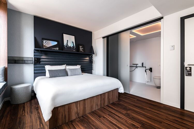 Wheelchair-accessible hotel room at A-Stay in Antwerp with a modern double bed, wood-effect flooring, sliding door and adapted bathroom with grab rails and roll-in shower.