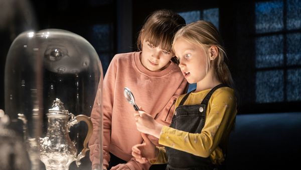Kinderen bekijken een zilverwerk met een vergrootglas