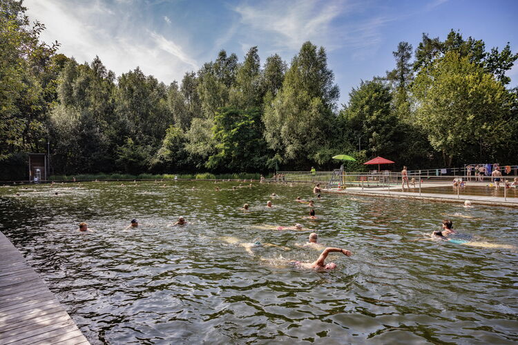 Besucher entspannen sich am Ufer des Schwimmteichs „Boekenberg“ in Antwerpen, der mit Naturwasser, Holzstegen und viel Grün rundherum aufwartet.