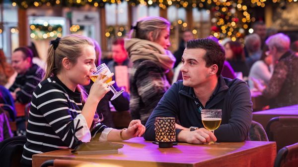 Ein Mann und eine Frau sitzen in einer Winterbar und nehmen einen Drink. Der Raum ist mit weihnachtlichen Accessoires geschmückt.