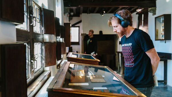 Een man met koptelefoon kijkt in een zaal van Museum Plantin-Moretus naar enkele museumstukken achter glas.