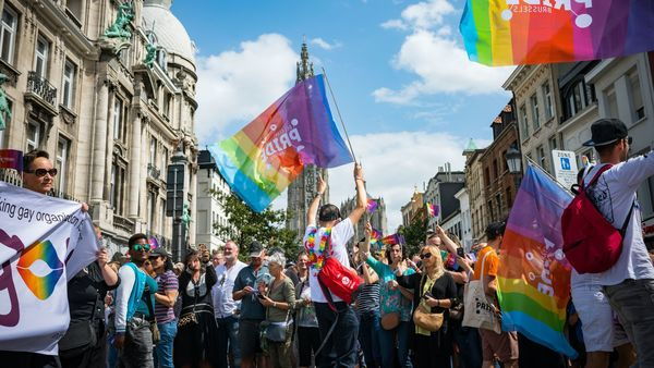 Several people stand outside in the centre of Antwerp and wave rainbow flags.