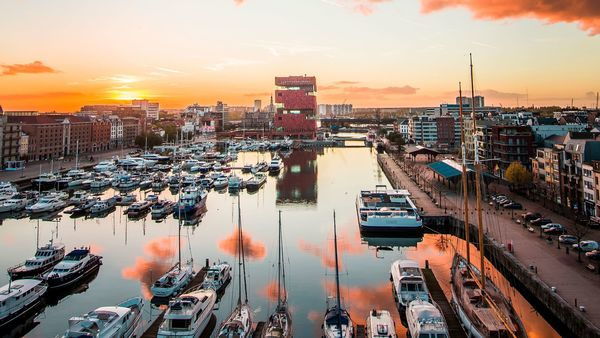 The red brick building of the MAS | Museum aan de Stroom towers out in the background. In the foreground are ships and sailboats in a dock.