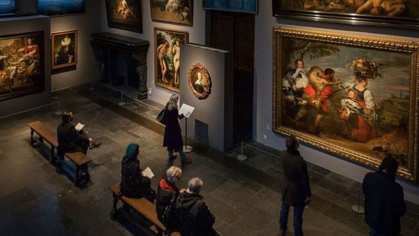 Mensen in een zaal vol verlichte schilderijen aan een grote muur