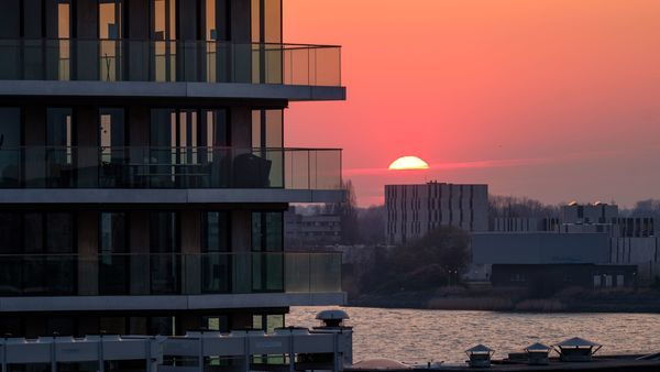 A modern apartment building, in the background the sunset, the Scheldt and the Left Bank (Linkeroever) district.