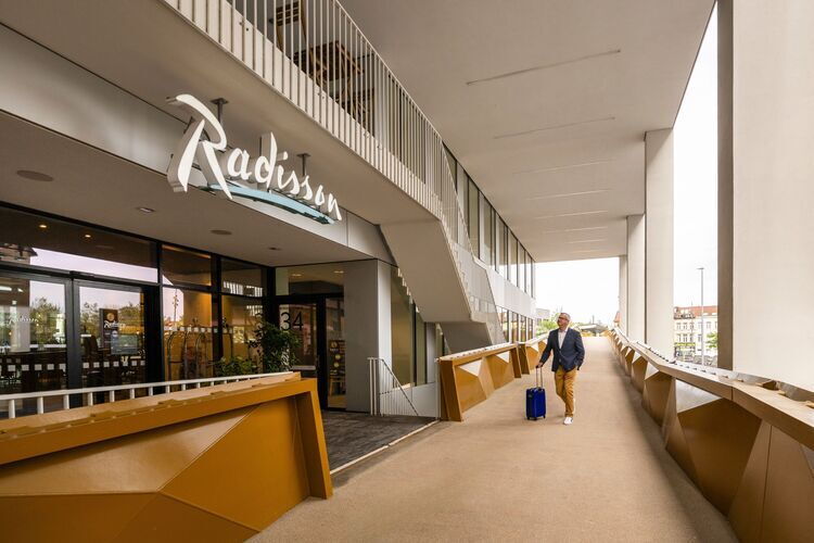 Man walking with suitcase in hand towards the reception desk of Radisson Hotel Antwerp Berchem.