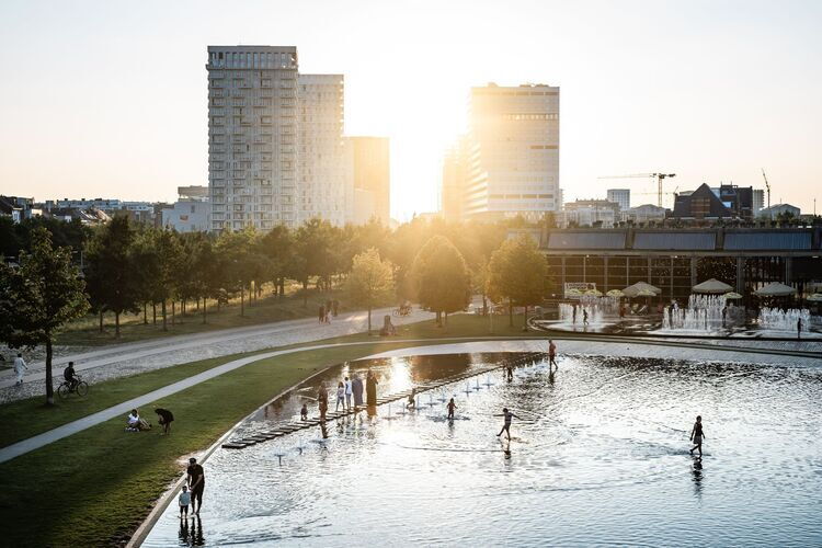 Wasserspielbereich im Park Spoor Noord mit seichtem Wasser, Springbrunnen und dem Park bei Sonnenuntergang.