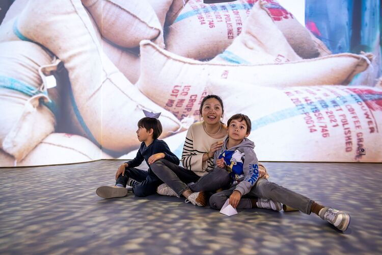Une femme est assise par terre avec deux enfants pendant qu'une projection lumineuse se déroule.