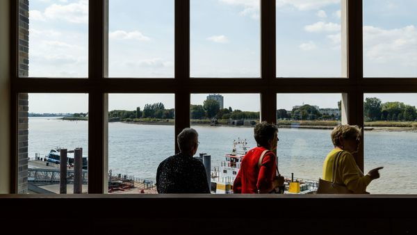 Drei Frauen betrachten das linke Ufer durch ein großes Fenster im Besucherzentrum