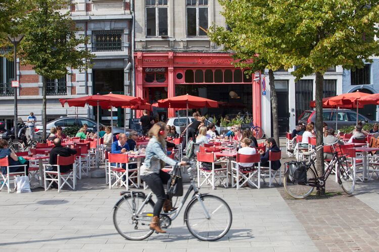Meisje dat fiets voorbij een terras vol met mensen.