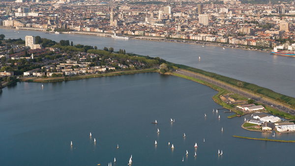 Aerial view of small sailboats in the water in a green neighbourhood. Next to them, the Scheldt and the Historic Centre of Antwerp.