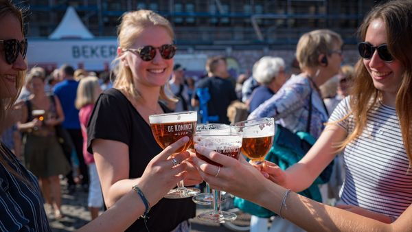 Several women toast outside with a bolleke of De Koninck beer in their hands.