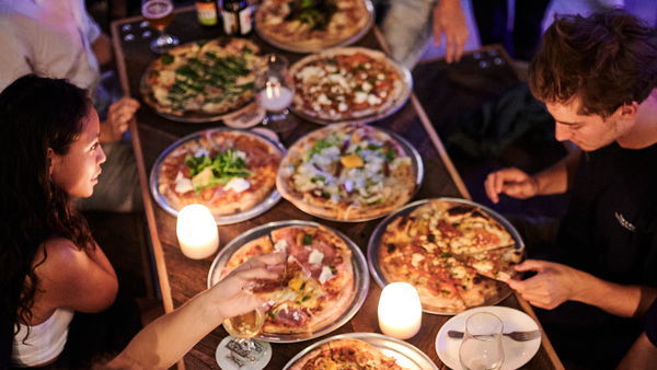 Vrienden rond de tafel genieten van heerlijke pizza's bij Otomat