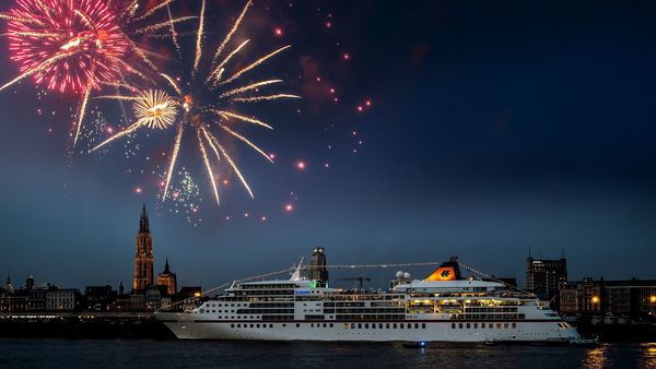 Cruise ship Europa sails on the Scheldt in the evening while fireworks are shot off.