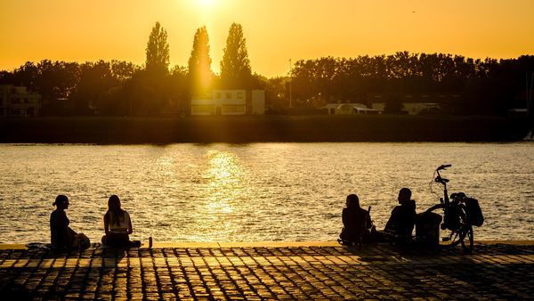 Mensen zitten aan de Scheldekaaien bij zonsondergang