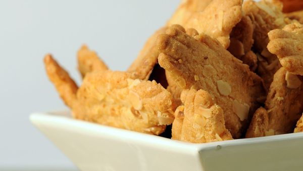 Een kommetje met een hoop zandkoekjes in de vorm van handjes. Op de koekjes zitten amandelschilfers