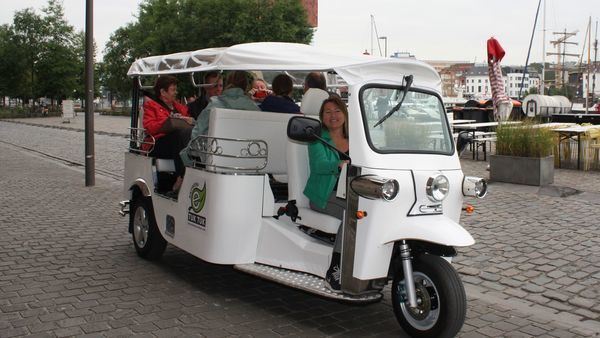 People sit in a white tuktuk - a motorised means of transport in which a number of people can be seated - that drives past the MAS | Museum aan de Stroom.