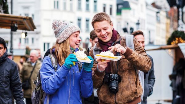 Ein Paar (Mann/Frau) ist winterlich gekleidet und genießt eine Waffel mit Schlagsahne auf dem Grote Markt in Antwerpen
