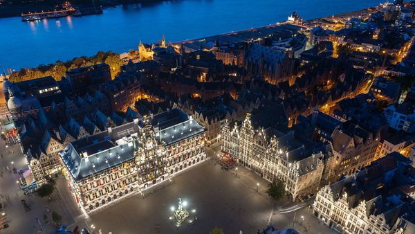 Una vista aérea del Ayuntamiento y la Plaza Mayor iluminados de noche. Al fondo se ve el río Escalda.