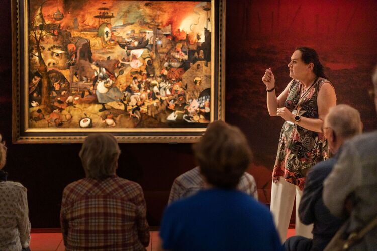  Standing guide explains the artwork Dulle Griet to a group of seated people.
