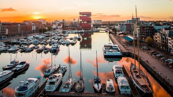 Several boats moored in the Willemdok at sunset. In the background, the red building of the MAS | Museum aan de Stroom stands out.