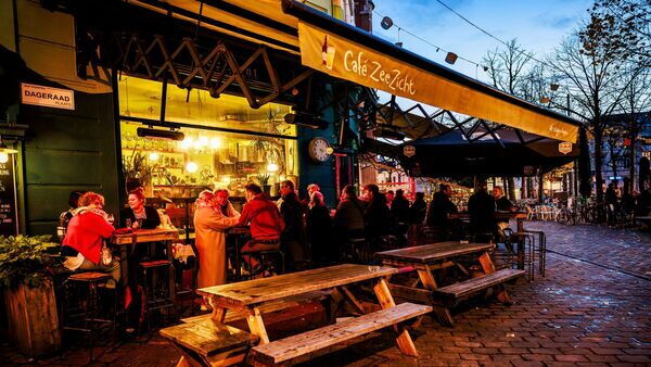 Tientallen mensen staan 's avonds buiten op het terras van café Zeezicht.