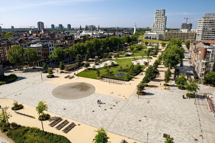 Luchtbeeld van het Zuidpark in Antwerpen met een groot open plein, wandelpaden, bomen en groene zones, omringd door woongebouwen en hoge torens, met de stad zichtbaar op de achtergrond.
