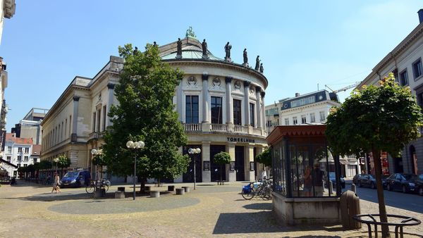 Un homme et une femme marchent bras dessus bras dessous sur une place avec un grand théâtre