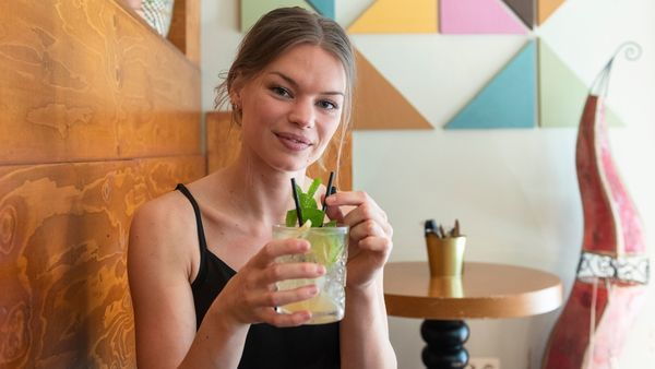 Chica con camiseta negra y un mojito en la mano en una mesa de madera