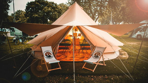 Two chairs stand in front of a tipi tent in green surroundings as the sun sets.