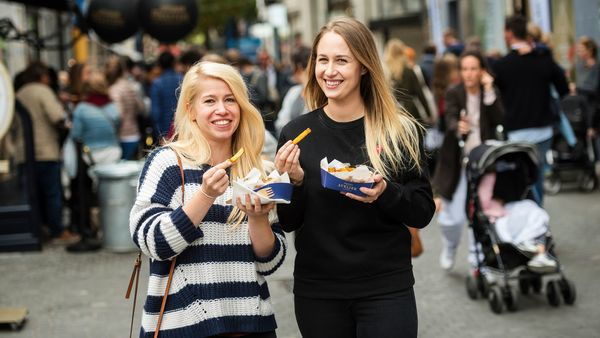 Deux femmes mangent des frites à l'extérieur et regardent la caméra.