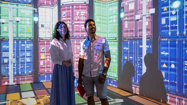 Vrouw en man kijken naar lichtprojectie van containers in de haven in the Antwerp Story