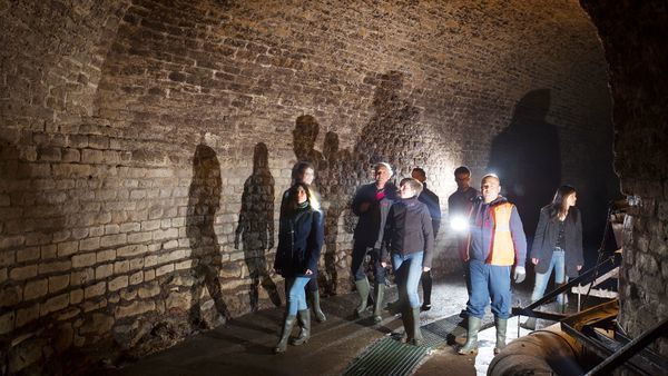 A group of people walk through an old tunnel with a torch.