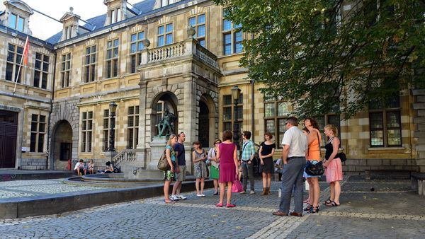 A group of people stand with guide in front of Heritage Library Hendrik Conscience and his statue.