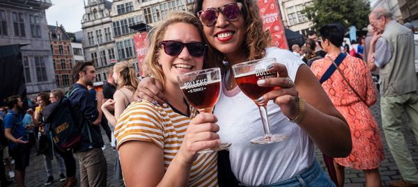 Twee vrouwen heffen op de Grote Markt hun glas Bollekes-bier.