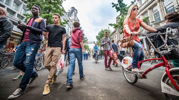 Several people stroll down shopping street de Meir, a woman is cycling on a red bike belonging to Velo, the city of Antwerp's shared bike system.