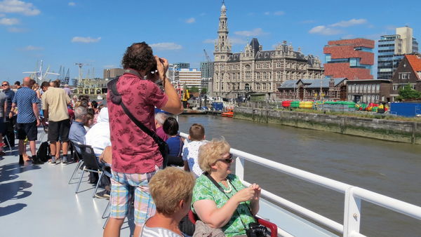 Some people on the deck of a ship enjoying the Antwerp skyline that includes the MAS | Museum aan de Stroom and the Loodswezen building.