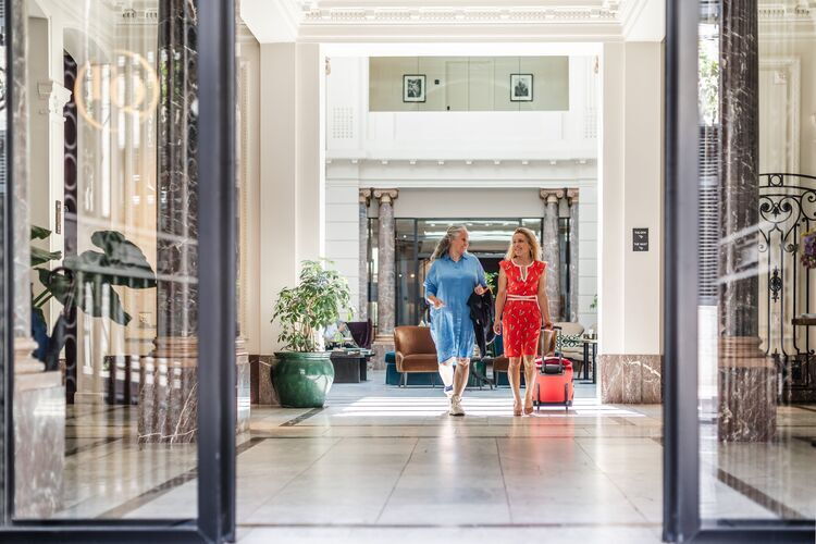 Two ladies are walking in the lobby of a hotel.