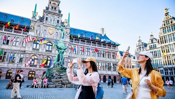 Two women take photos on the Grote Markt square. In the background the town hall and the statue of Brabo.
