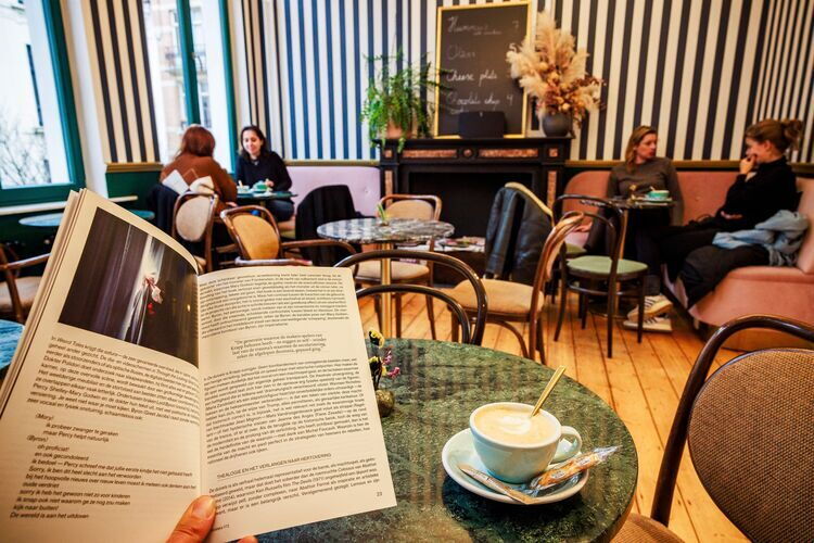 Une dame avec un livre à la main savoure un café.