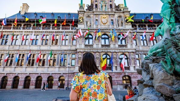 Grote Markt, dame staat naast het standbeeld van Brabo en kijkt naar het Stadhuis dat versierd is met vlaggen