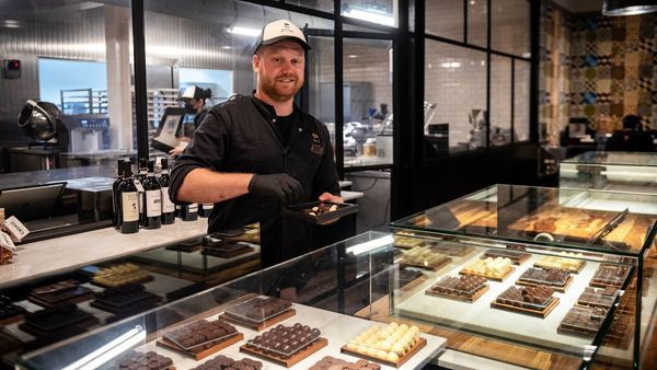 Ein Chocolatier füllt eine Pralinenschachtel hinter einer Theke voller Schokolade.