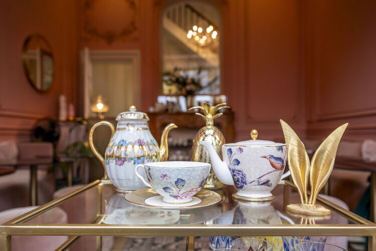 Elegante theeserviezen en gouden decorstukken staan uitgestald op een chic tafelblad in een stijlvol, roze interieur bij Domestic Bakkerij & High tea.