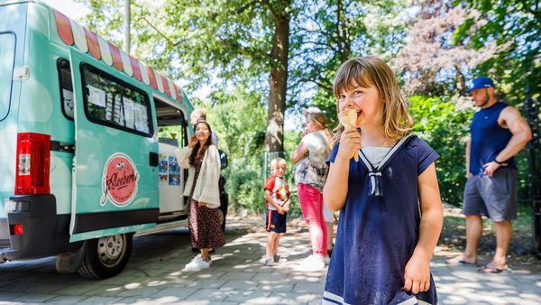 Meisje eet ijsje aan ijsjeskraam in het park.