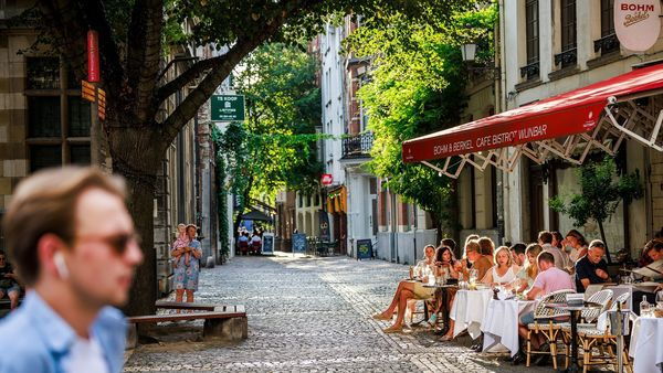 Man walks past terraces on Hendrik Conscienceplein where customers enjoy a drink