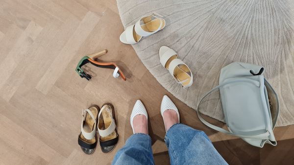 Verschillende paren sandalen en een handtas op een houten vloer
