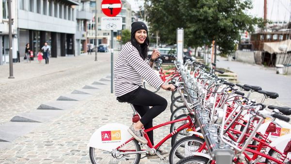 Vrouw zit op een Velo bij een Velostation.