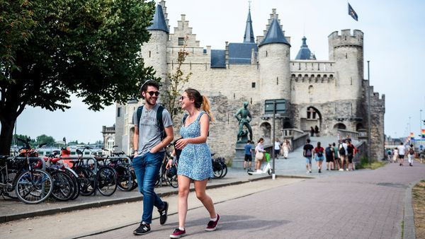 A man and a woman walk smiling past the medieval castle and visitor centre Het Steen.